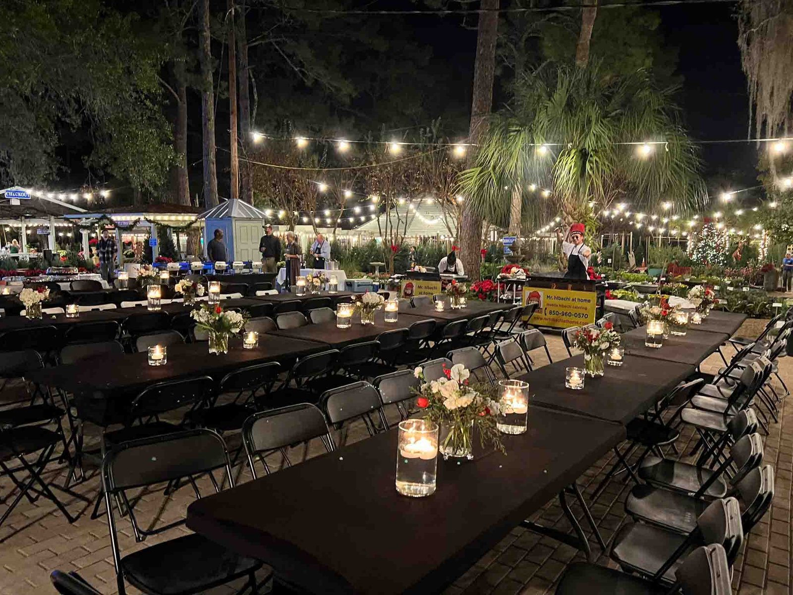 Guests at long tables under string lights at a nighttime hibachi dinner