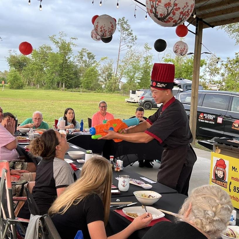 Hibachi chef with a water gun at an outdoor party under lanterns