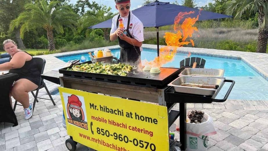 Hibachi chef cooking with flames at a poolside grill cart