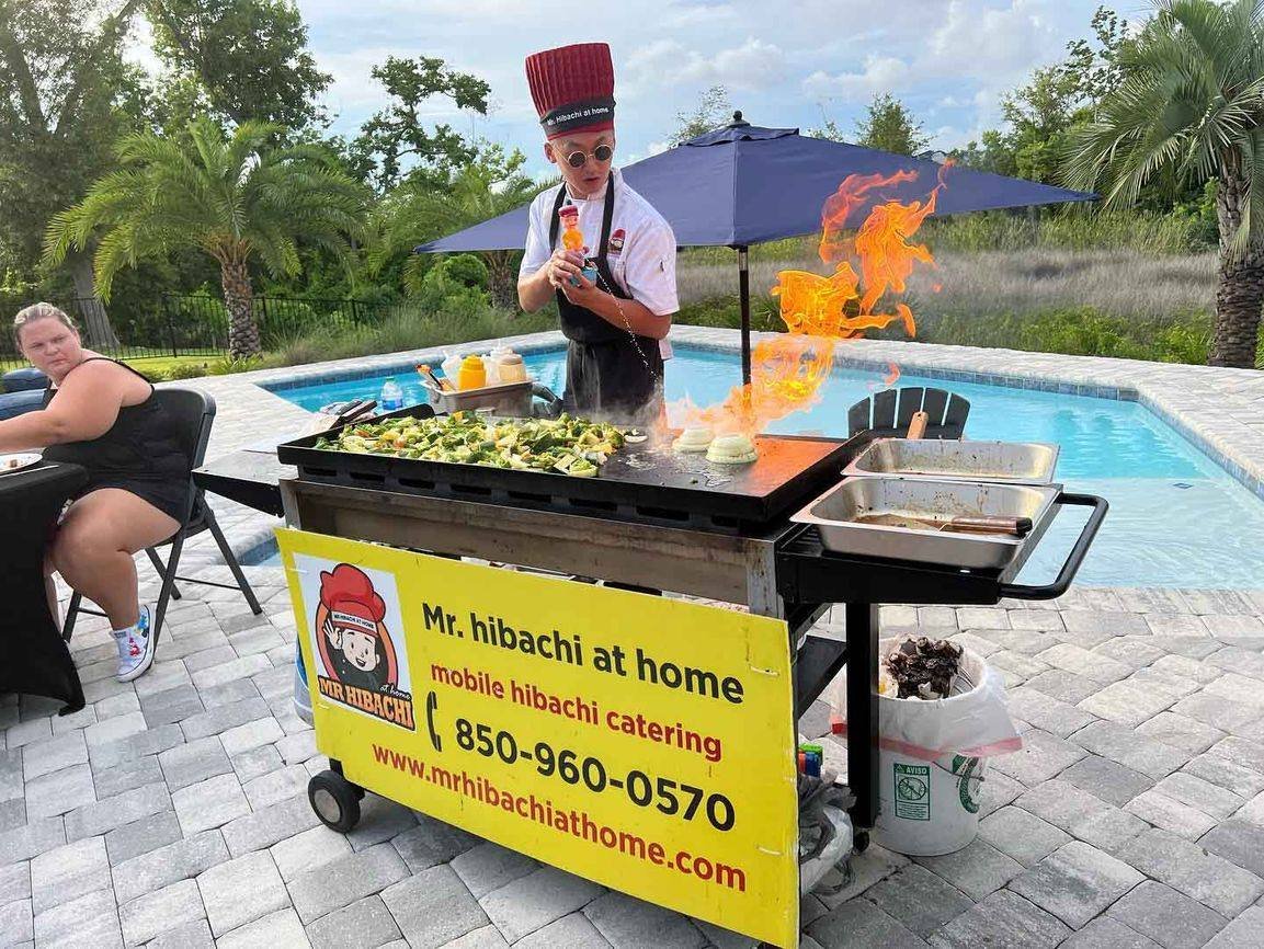 Hibachi chef cooking with flames at a poolside grill cart