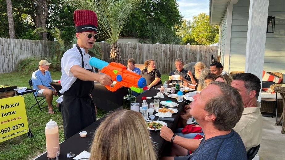 Hibachi chef with a water gun entertaining guests at an outdoor table