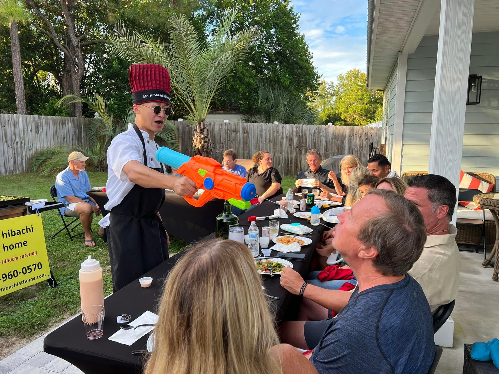 Hibachi chef with a water gun entertaining guests at an outdoor table