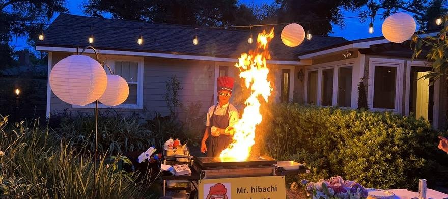 Hibachi chef cooking with flames in a backyard at night