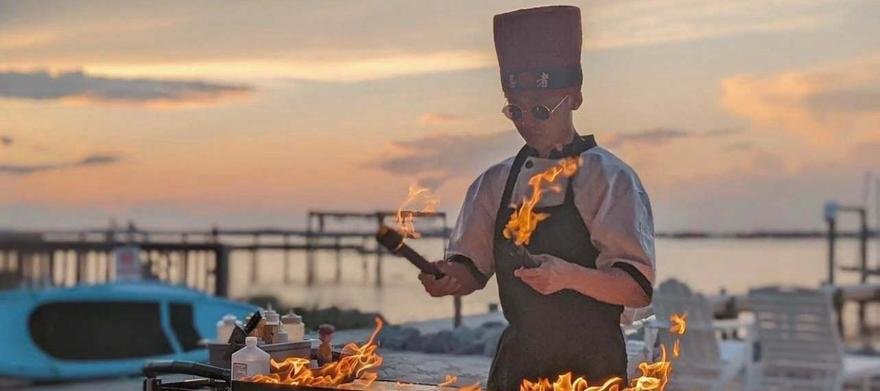 Hibachi chef cooking with flames at sunset by the water