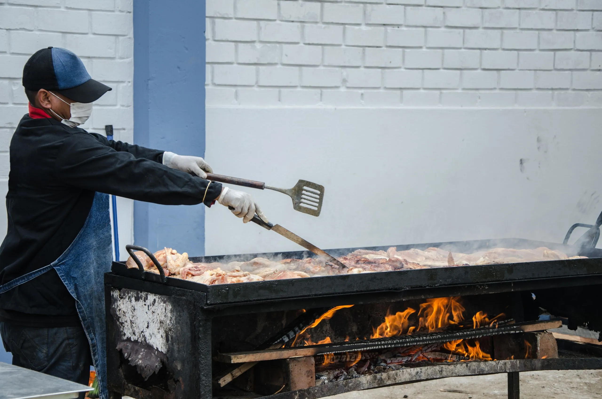 Cook grilling meat over an open-flame grill